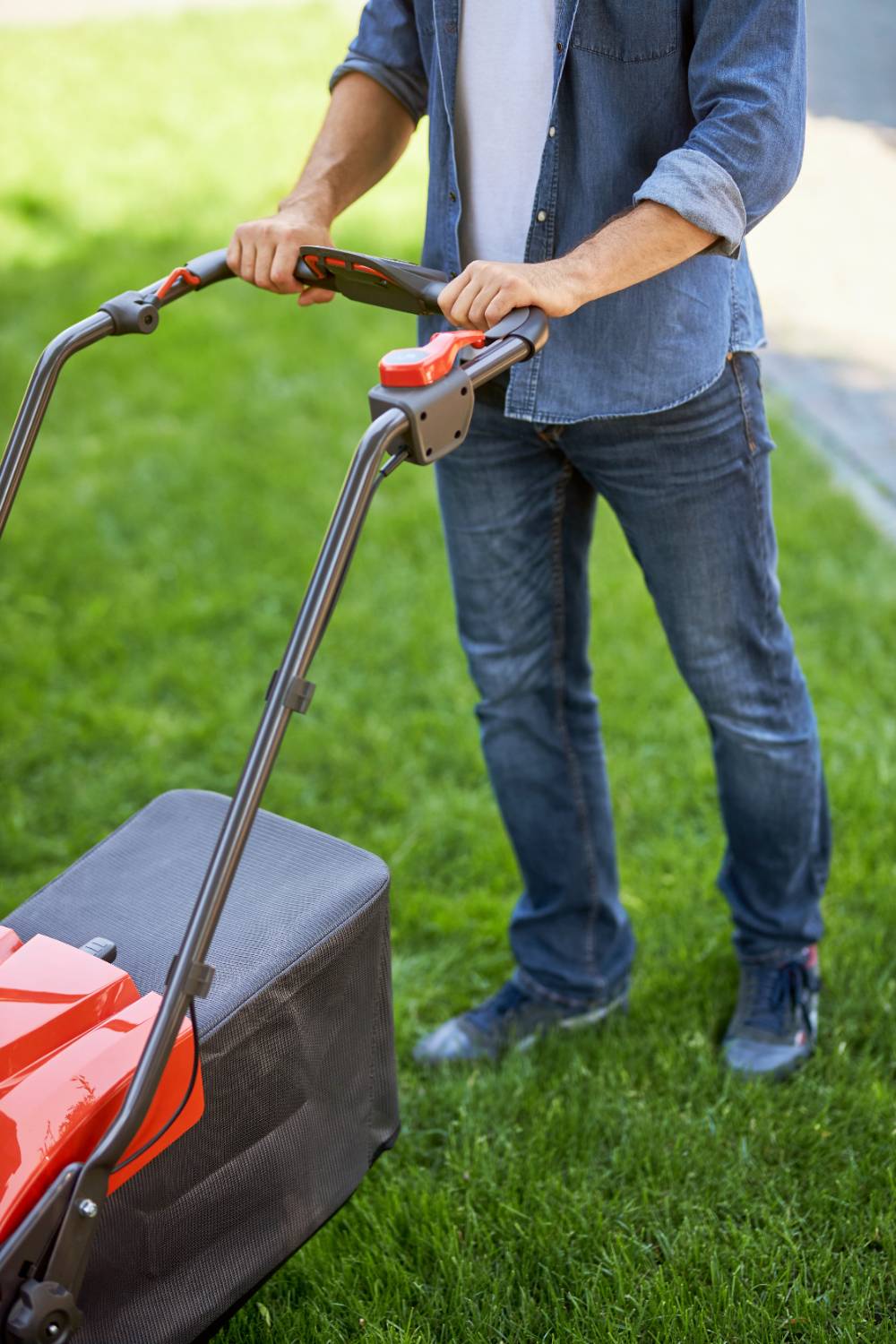 Unrecognizable male gardener pushing modern lawn mower while walking on grass above view of handyman